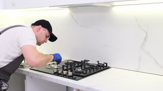 A gas engineer repairs a gas stove in the kitchen. The call of the master gas fitter to the house. 4k video